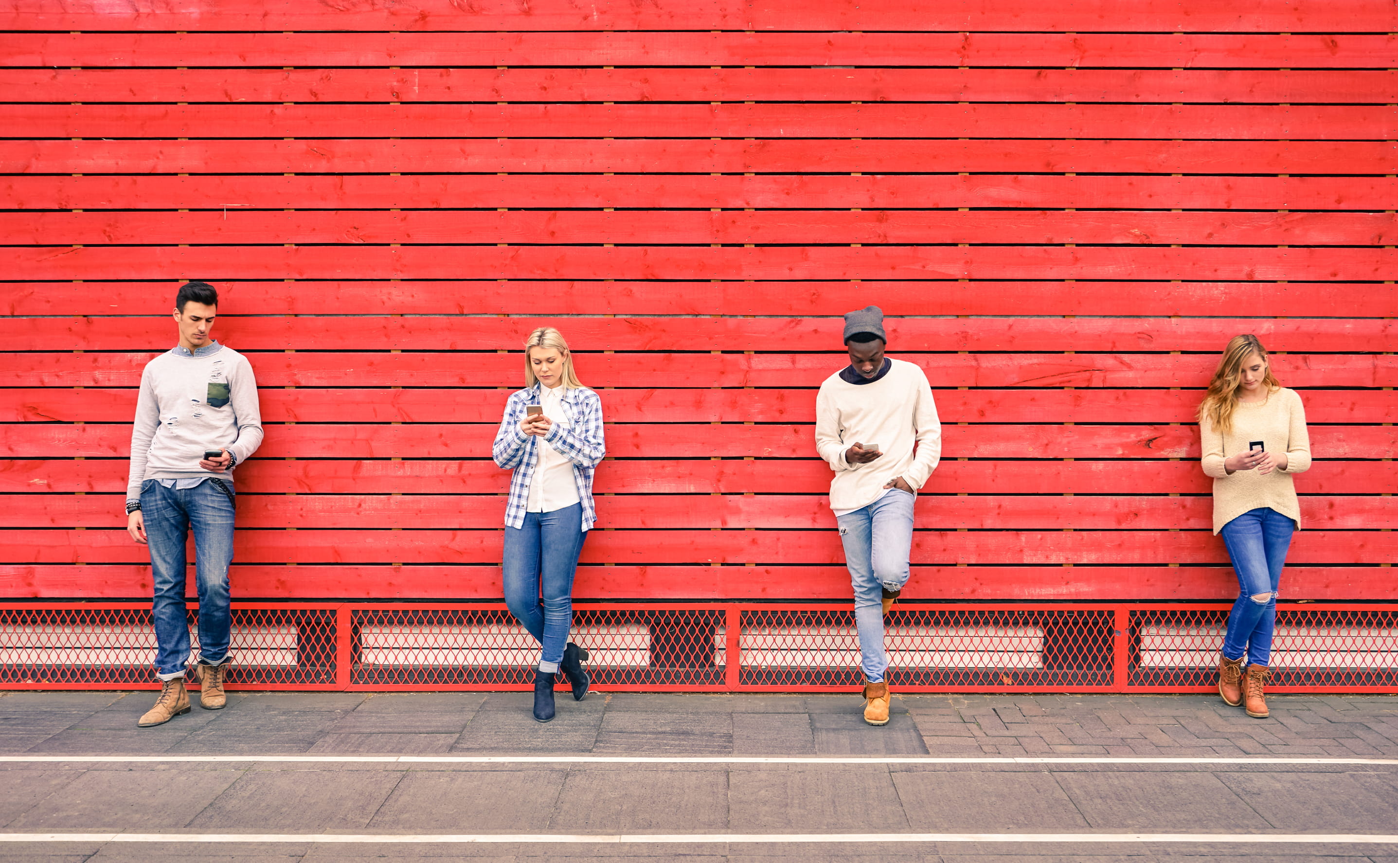 people on their phones leaning against red wall people on their phones leaning against red wall